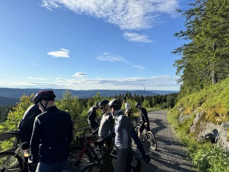 Gravel riders stopped on a forest road high in the Nordmarka above Oslo, with forested ridgelines running to the horizon