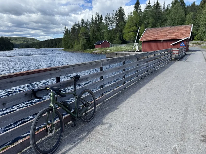 A green gravel bike leaning against the rail of a dam in the Nordmarka near Ullevålseter