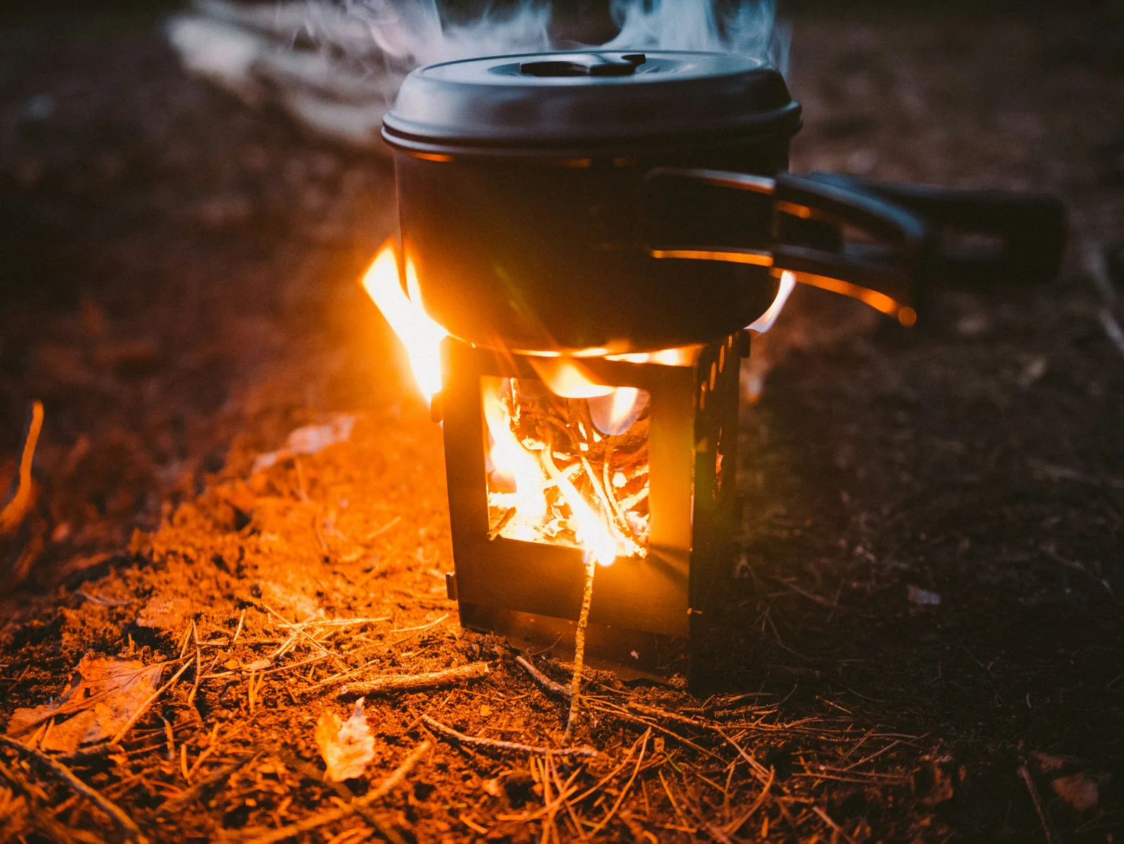 A camping pot steaming over a small wood-fired stove at dusk